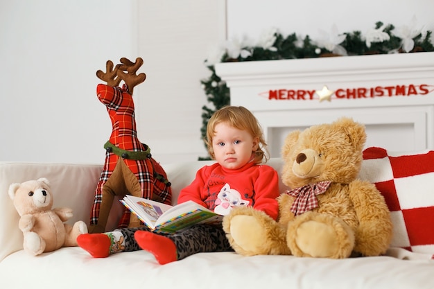 Little baby girl reading a book in his toys Christmas decorations