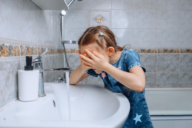 小さな女の赤ちゃんが朝に元気を出すために冷たい水で顔をすすぎます水洗いの手順