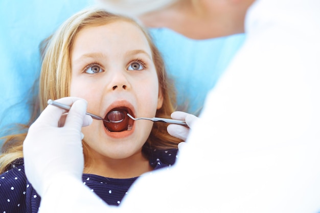 Photo little baby girl sitting at dental chair with open mouth during oral check up while doctor. visiting dentist office. medicine concept. toned photo.