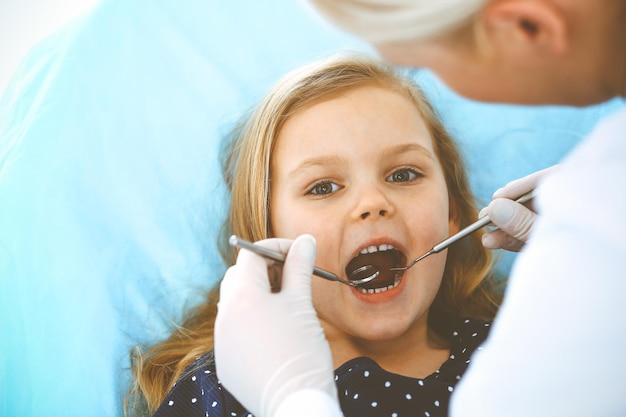 Bambina seduta alla poltrona del dentista con la bocca aperta durante il controllo orale mentre il medico. visita allo studio dentistico. concetto di medicina. foto tonica.