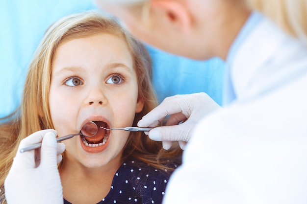 Little baby girl sitting at dental chair with open mouth during oral check up while doctor. Visiting dentist office. Medicine concept. Toned photo.