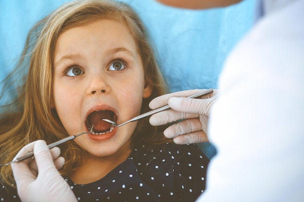 Little baby girl sitting at dental chair with open mouth during oral check up while doctor. Visiting dentist office. Medicine concept. Toned photo.