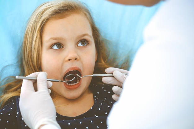 Little baby girl sitting at dental chair with open mouth during oral check up while doctor. Visiting dentist office. Medicine concept. Toned photo.