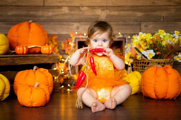 Little baby girl sitting with pumpkins in a bright orange dress on a brown background, halloween