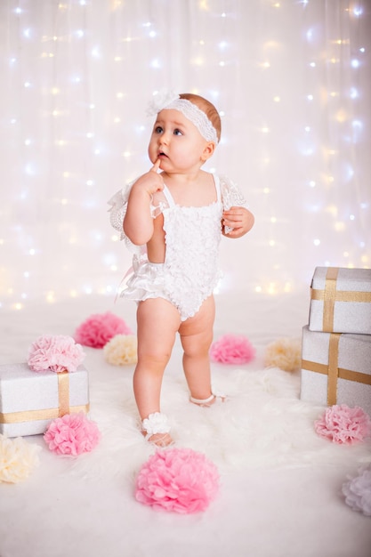 Little baby girl staying among a lot of gift boxes celebrating birthday or christmas