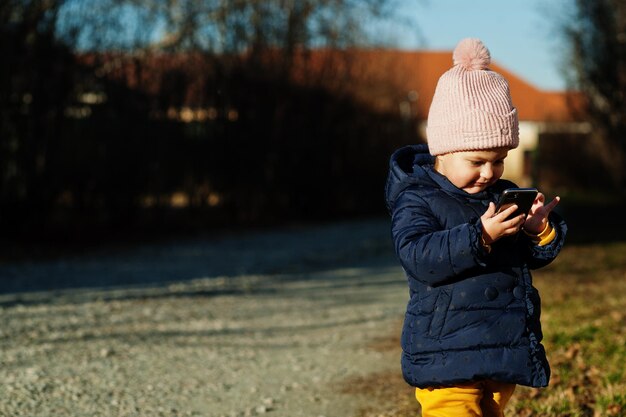 Little baby girl in the sunny day hold mobile phone in hands