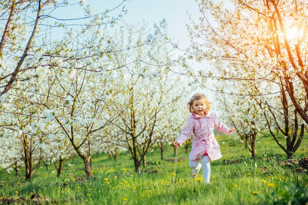 Маленькая девочка, которая бежит между цветущих деревьев на закате. Арканзас