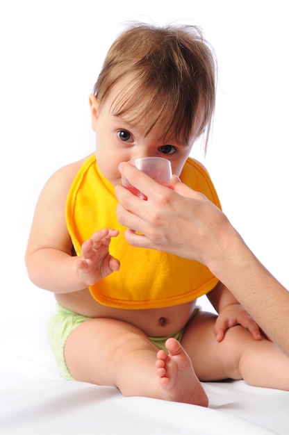 Little baby girl with bib looking at camera and drinking water or compote from cup.