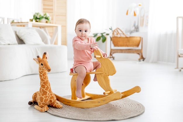 Little baby at home in the children's bright room swinging on a wooden rocking horse the child is playing at home