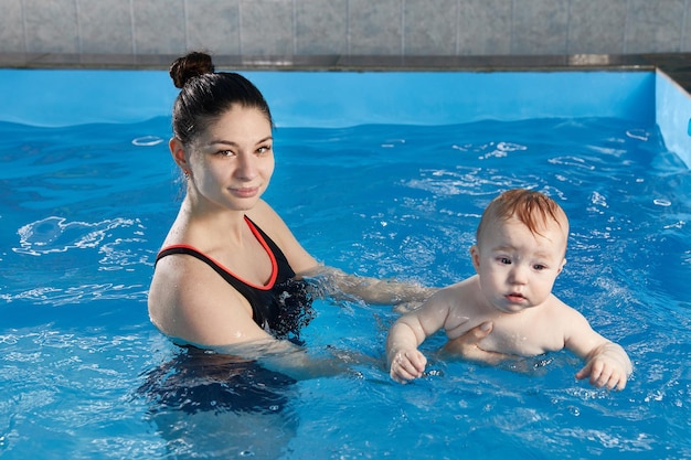 小さな赤ちゃんが教師とプールで泳ぐことを学ぶ