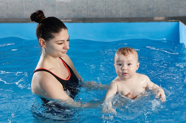 Foto piccolo bambino che impara a nuotare in piscina con l'insegnante