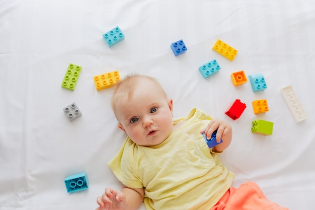 Little baby lying on white linen between toys