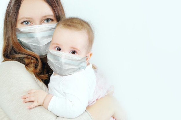 Little baby and mother in medical protective face mask on white background