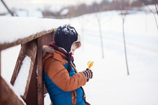 Little Baby playing and eating sweet cockerel in winter day. Kids play in snowy forest.