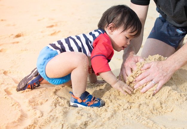 写真 夏の休日のビーチで両親と砂を遊ぶ小さな赤ちゃん