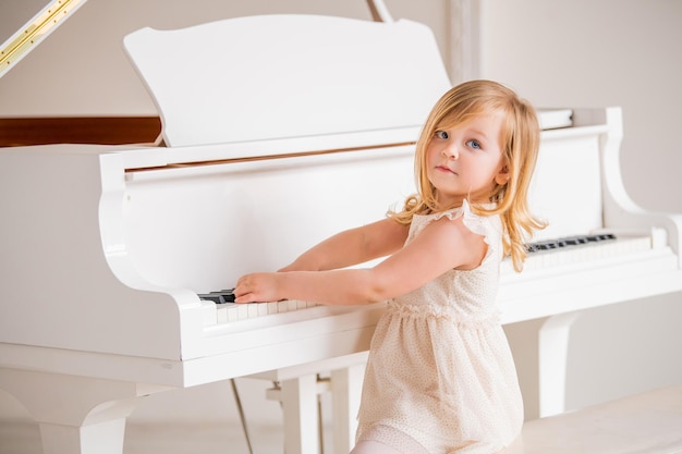 A little baby plays a big white piano in a bright sunny room