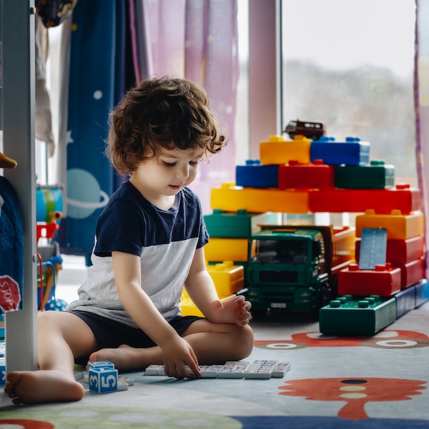 Little baby plays dominoes in his room on the floor