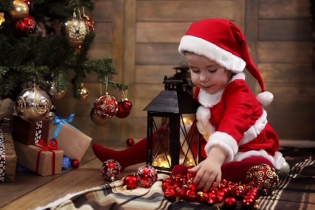 Piccolo bambino seduto per terra nella stanza davanti a un albero di natale decorato