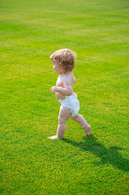 Little baby walking in the summer park in diaper pants first step