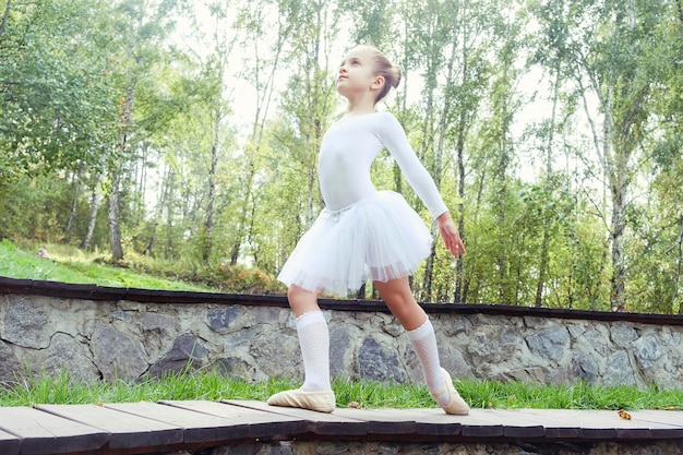 Little ballerina girl shows elements of choreography on a summer day on a path in the park