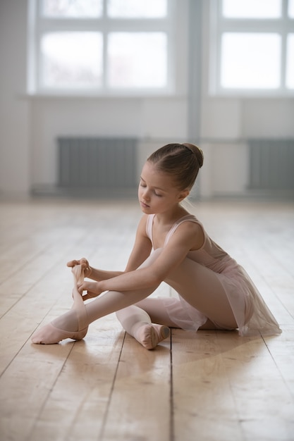 Little ballerina sitting on the floor and preparing for the classes in dance studio