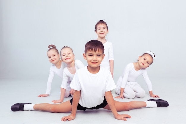 Piccole ballerine e ballerun per bambini che fanno esercizi e si siedono sul pavimento in una lezione di balletto bianco.