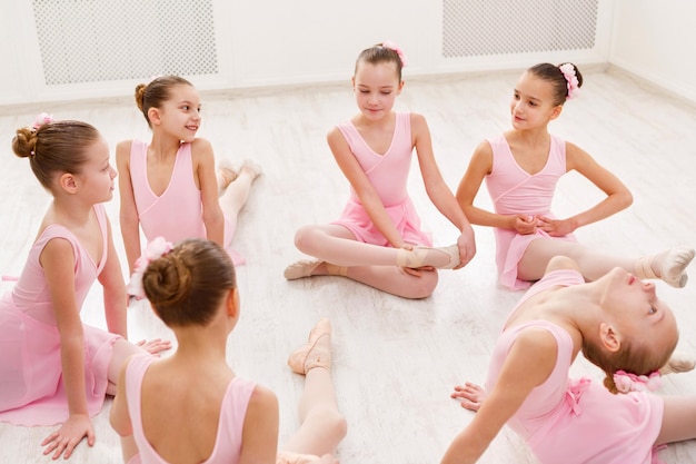 Little ballerinas talking in ballet studio. Group of girls having break in practice, sitting on floor. Classical dance school