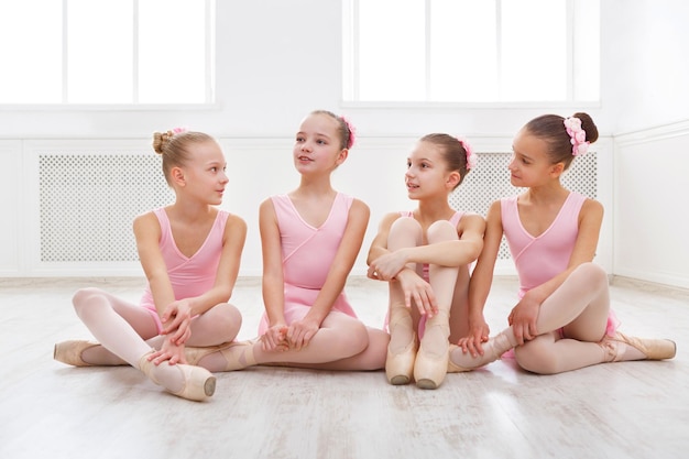 Little ballerinas talking in ballet studio. Group of girls having break in practice, sitting on floor. Classical dance school