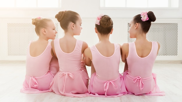 Little ballerinas talking in ballet studio. Group of girls having break in practice, sitting on floor. Classical dance school