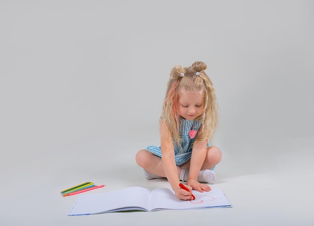 Photo a little beautiful blonde girl draws on a white background