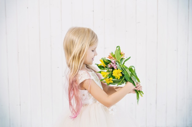 Bambina bellissima bambina in bellissimo vestito con bouquet di fiori su fondo di legno bianco