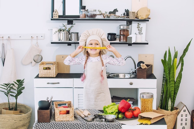 Little beautiful child girl cook in the kitchen with different vegetables and spaghetti