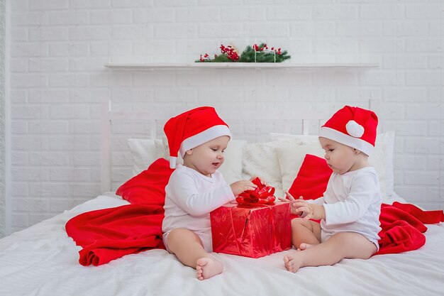 사진 어린 소년과 소녀가 크리스마스 모자를 쓰고 침대에 앉아 있다