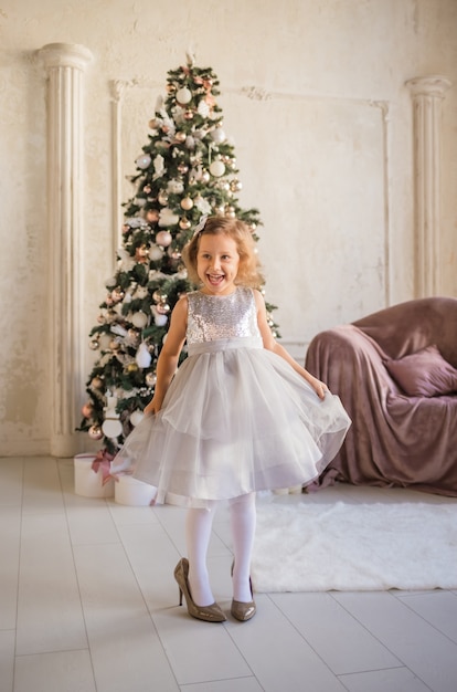 Little beautiful girl in big shoes dancing near the Christmas tree