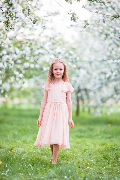 Little beautiful girl enjoying smell in a flowering spring garden