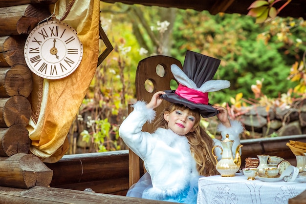 Little beautiful girl holding cylinder hat with ears like a rabbit over head at the table