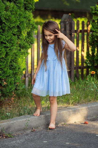 写真 夏に緑の背景の路上で裸足で青いドレスを着た美しい少女