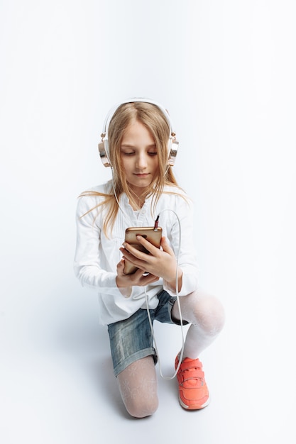 Little beautiful girl, listening to music and looking at the phone