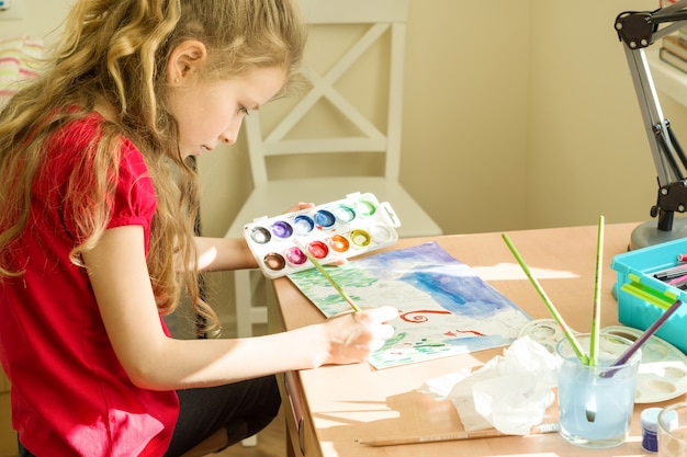 Photo little beautiful girl painting with watercolors, sitting at home at the table