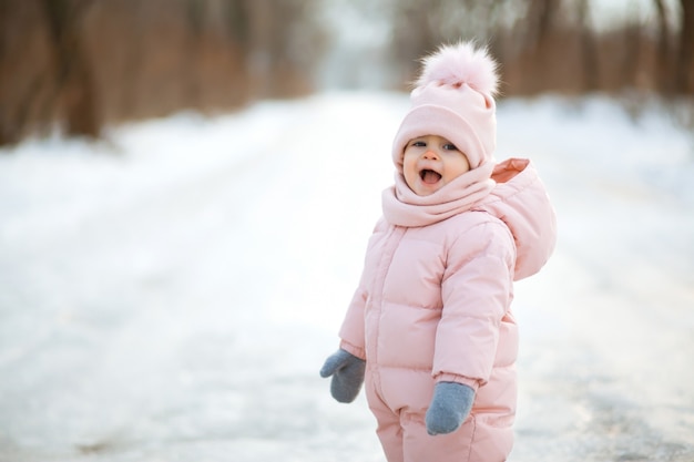 雪に覆われた冬の公園でピンクのジャンプスーツで美しい少女