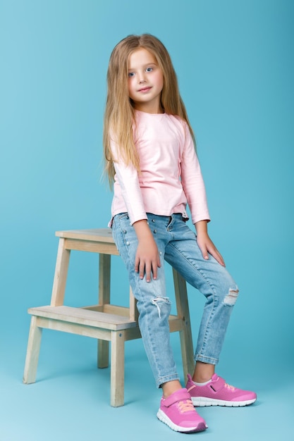 Little beautiful girl in pink sweater and jeans posing in studio