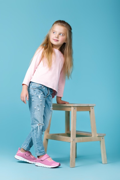 Little beautiful girl in pink sweater and jeans posing in studio