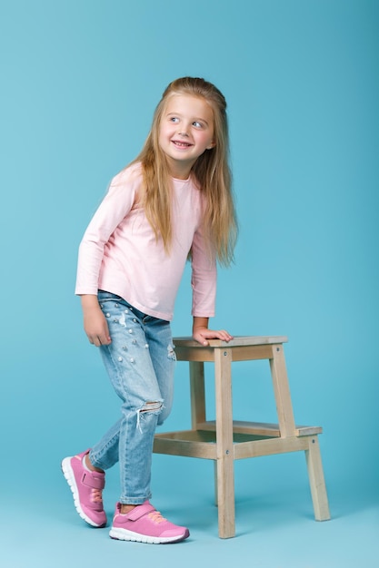 Little beautiful girl in pink sweater and jeans posing in studio