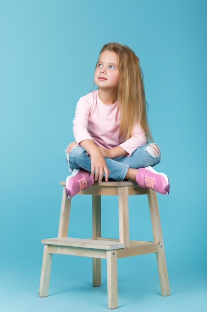 Little beautiful girl in pink sweater and jeans posing in studio