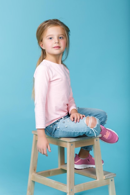 Little beautiful girl in pink sweater and jeans posing in studio