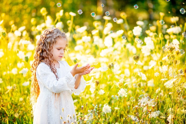 Little beautiful girl playing on the lawn in summer with soap bubbles