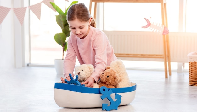 Little beautiful girl sitting on the floor and playing with toy ship in sunny room