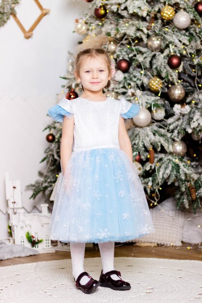 Little beautiful girl in a smart dress stands near the Christmas tree