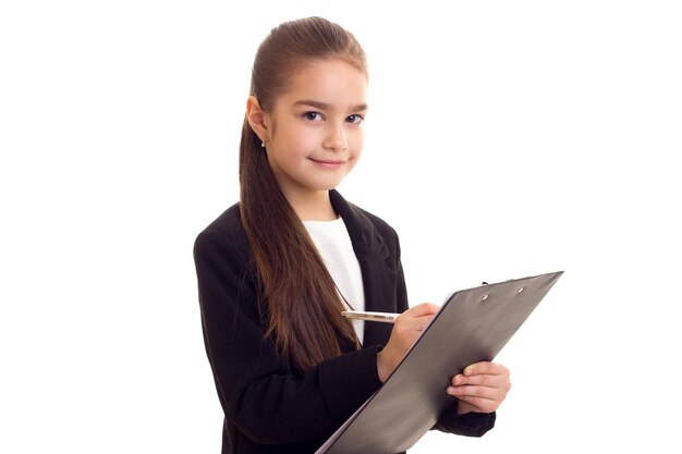 Little beautiful girl in Tshirt and jacket holding pen and folder on white background in studio