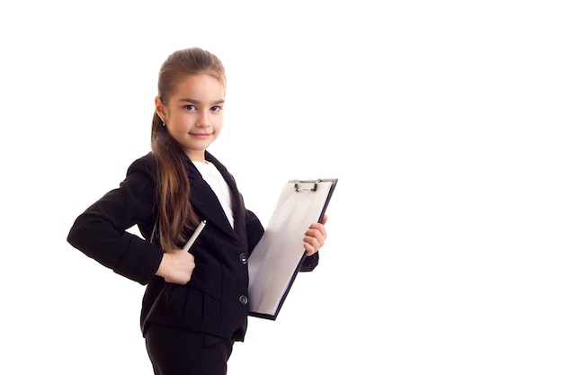 Little beautiful girl in Tshirt and jacket holding pen and folder on white background in studio